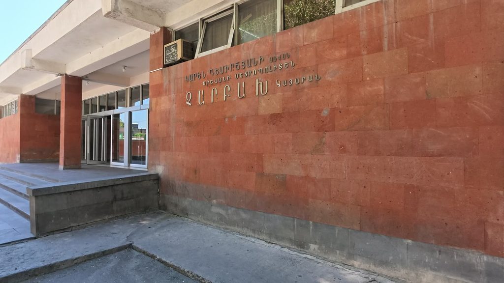 The entrance of Charbakh metro station: a wall of red tuff blocks carrying the station's name in Armenian letters, beside glass doors at the top of a few steps.