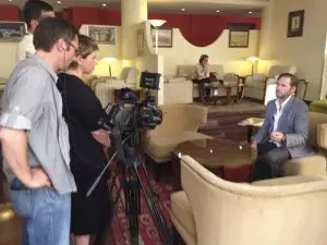 Director Christopher Chambers answering questions during a television interview at the Royal Tulip Grand Hotel.