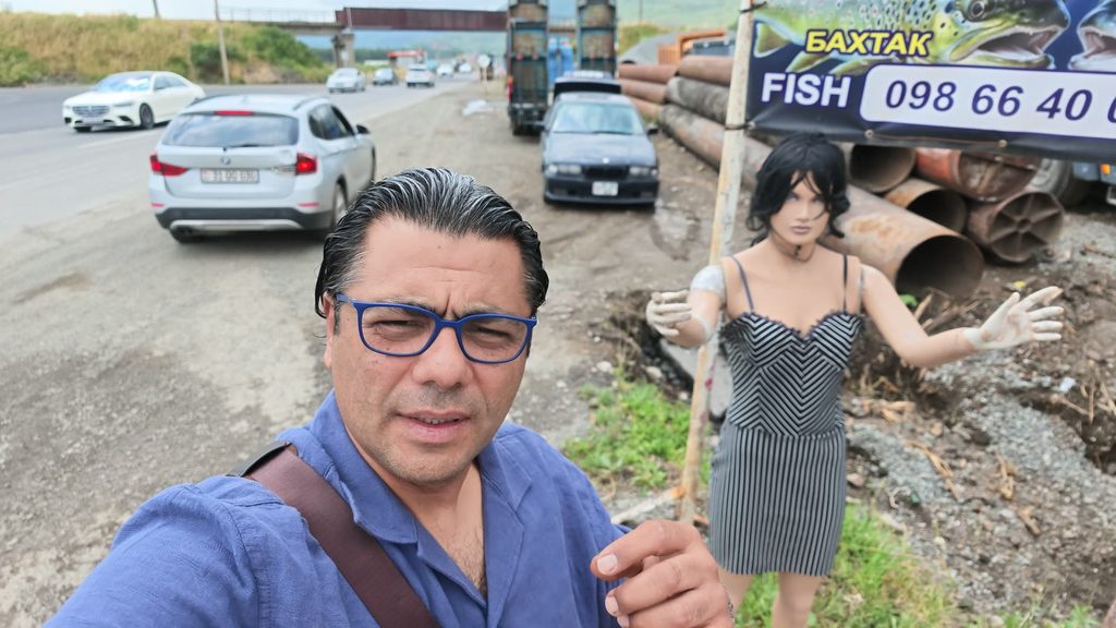 Roadside fish stalls with hand-painted signs, a mannequin standing among them.