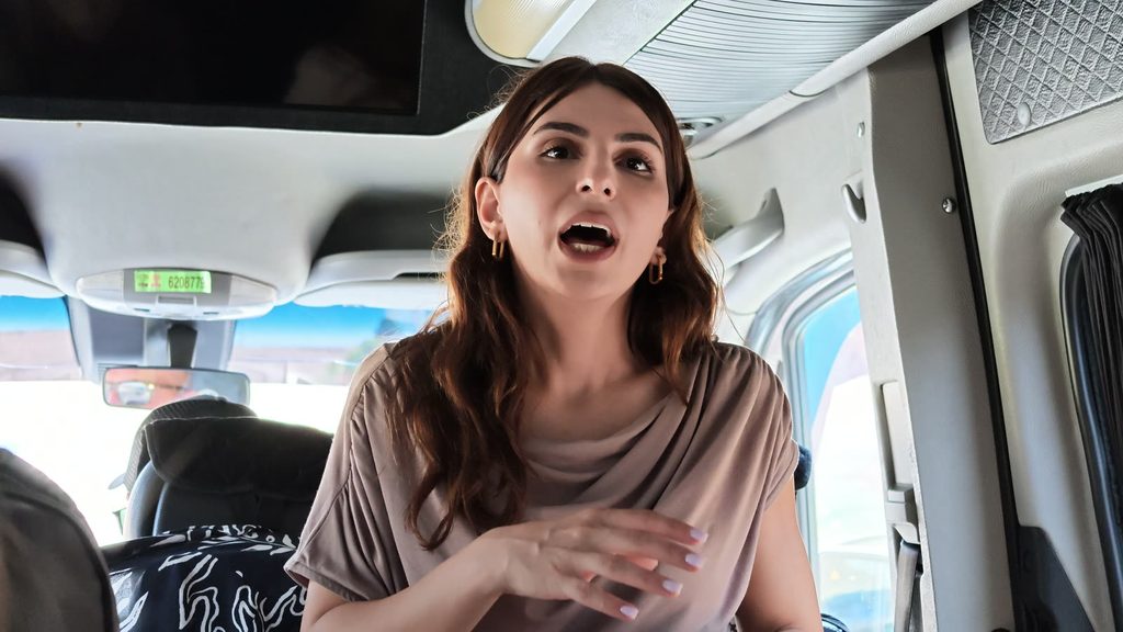 Karina standing at the front of the minibus with a microphone, passengers seated behind her.
