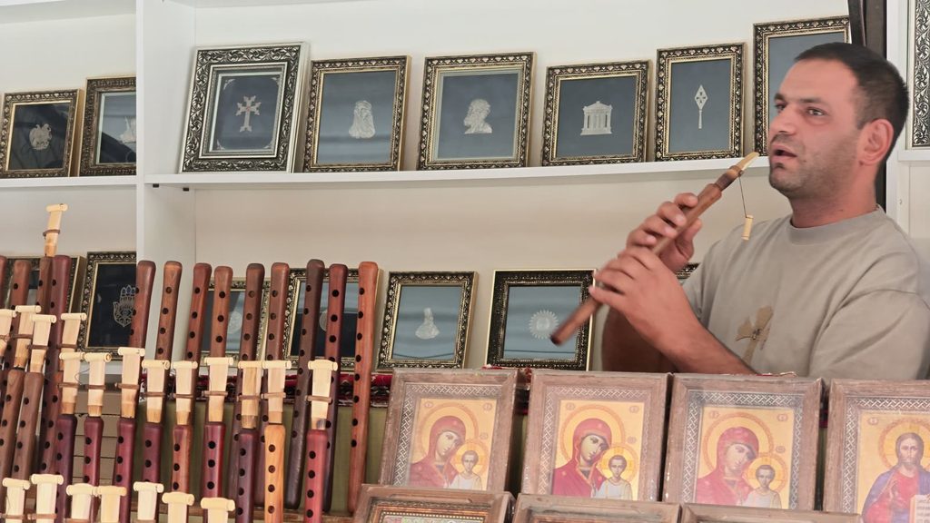 A man playing a duduk behind a stall of icon paintings.
