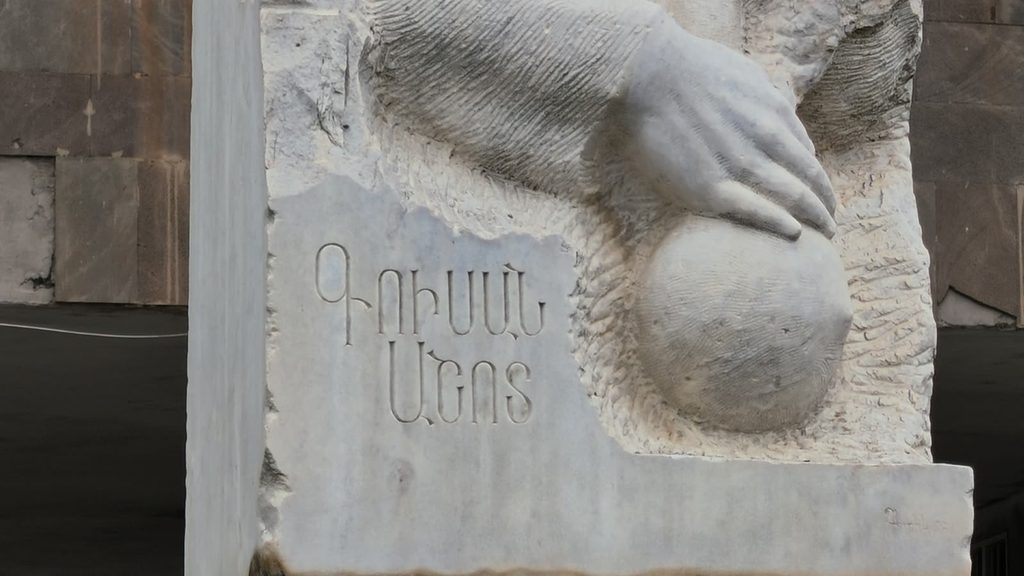 A carved stone hand resting on a sphere beside the Armenian inscription for Gusan Ashot, a detail of his monument in Goris.