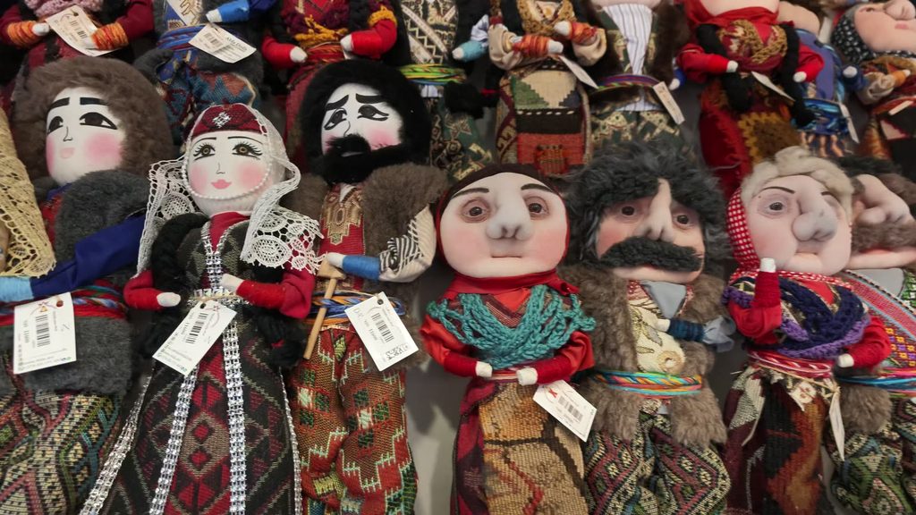 Rows of small cloth dolls in traditional Armenian dress on a market stall.
