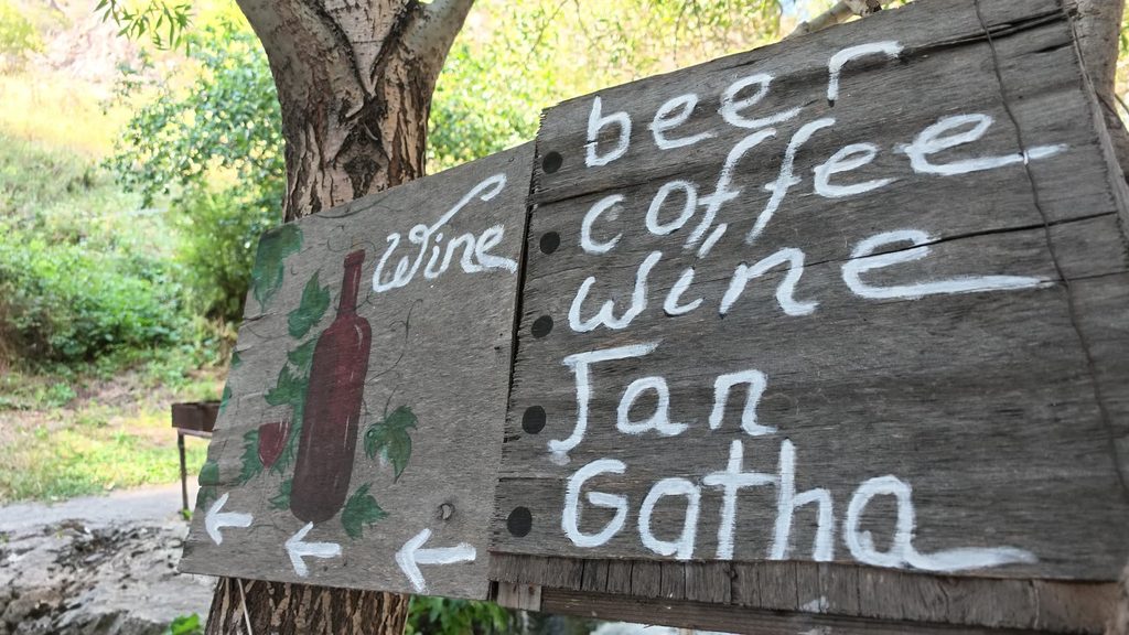 A small kiosk at the foot of the waterfall with a hand-painted sign.