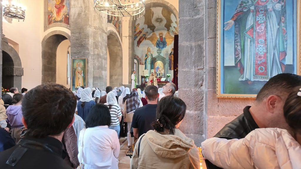 A packed church during a service, with women in white lace veils facing a painted altar where a priest serves.