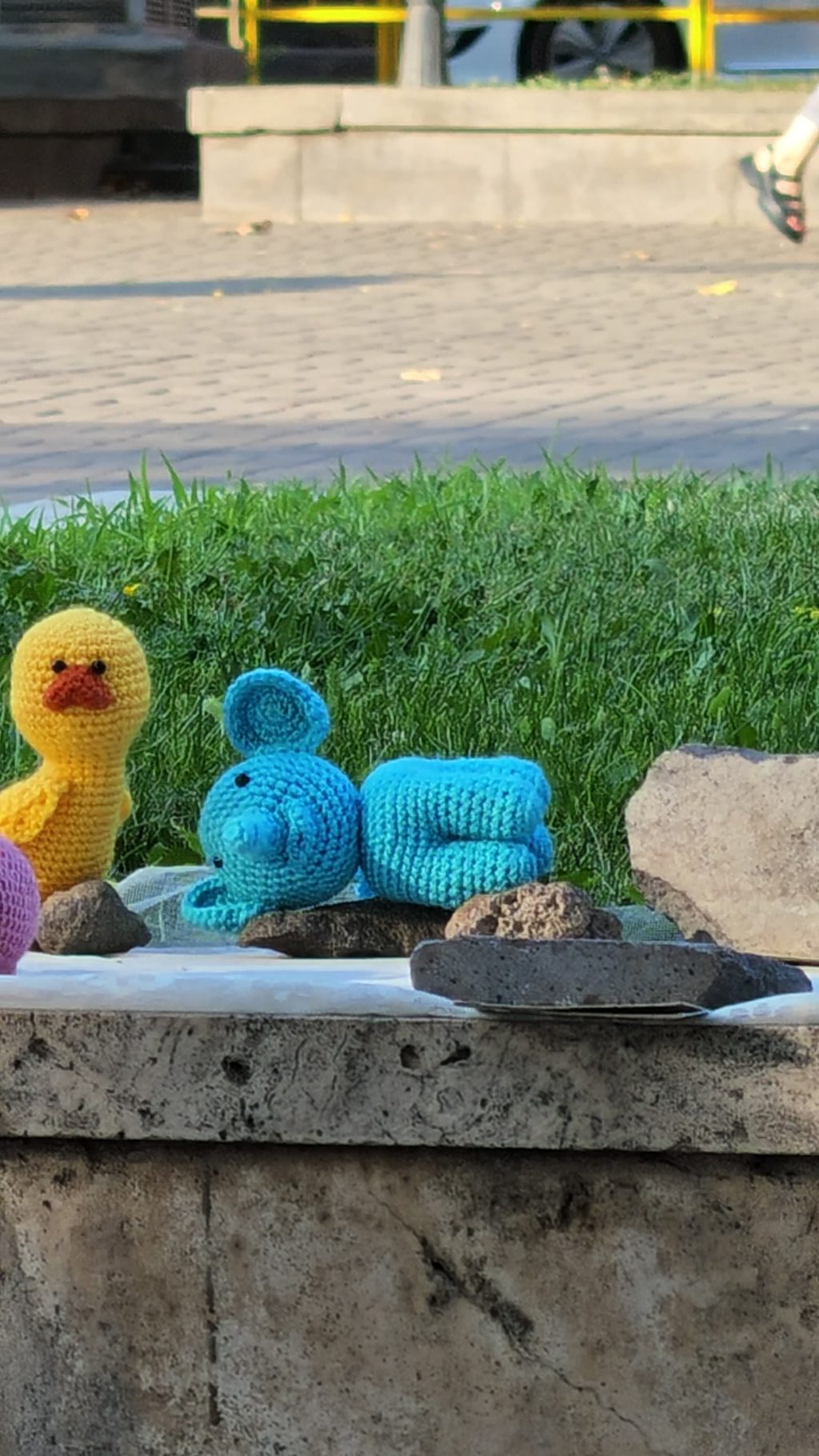Crocheted toys lined up on a stone ledge - a duck, a blue creature, a pink pig.