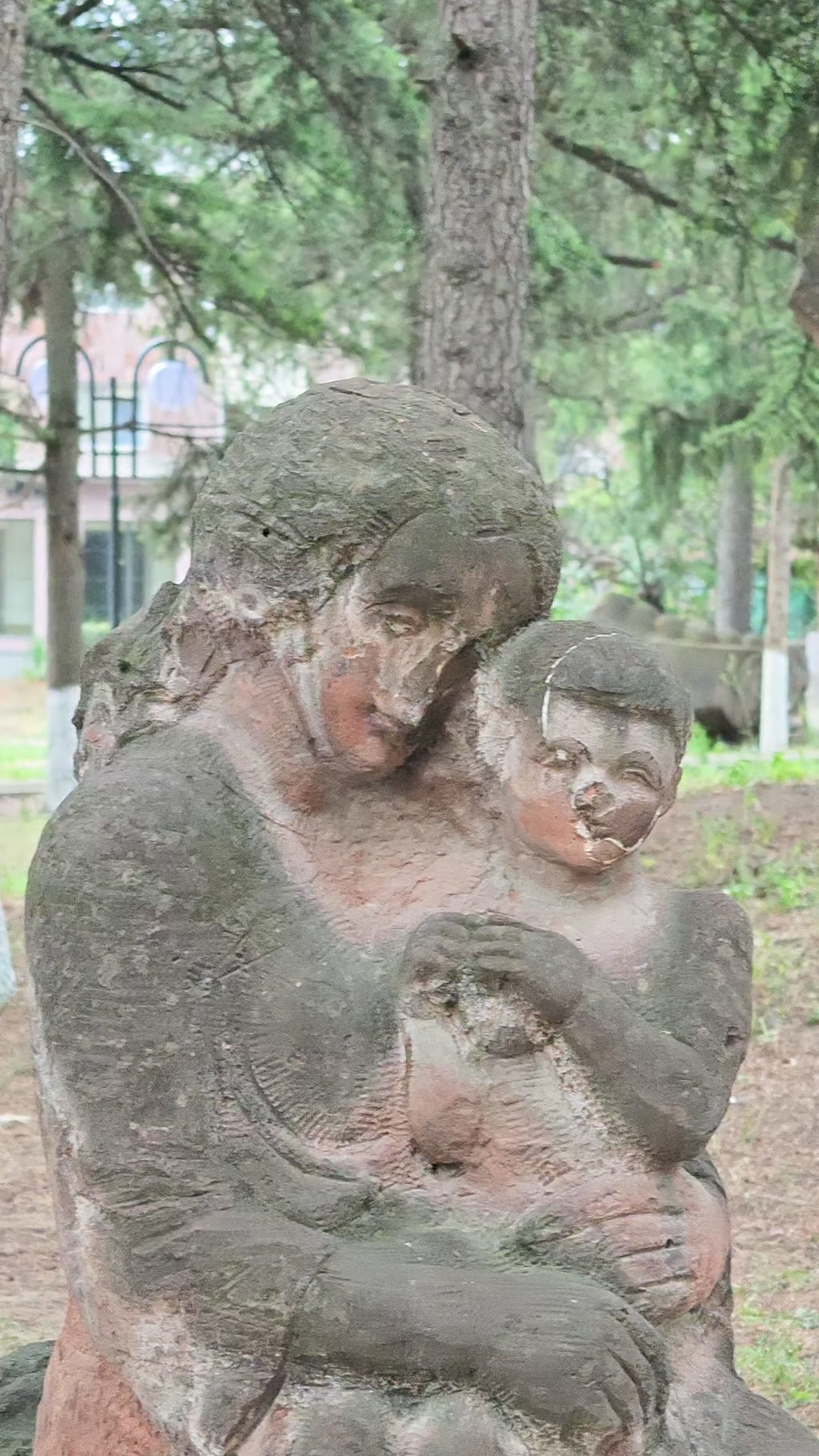 A mother and child carved from volcanic tuff, standing among trees.