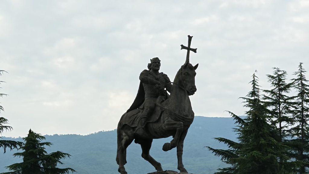 A dark statue of a rider on a rearing horse holding a cross, silhouetted on a ridge.