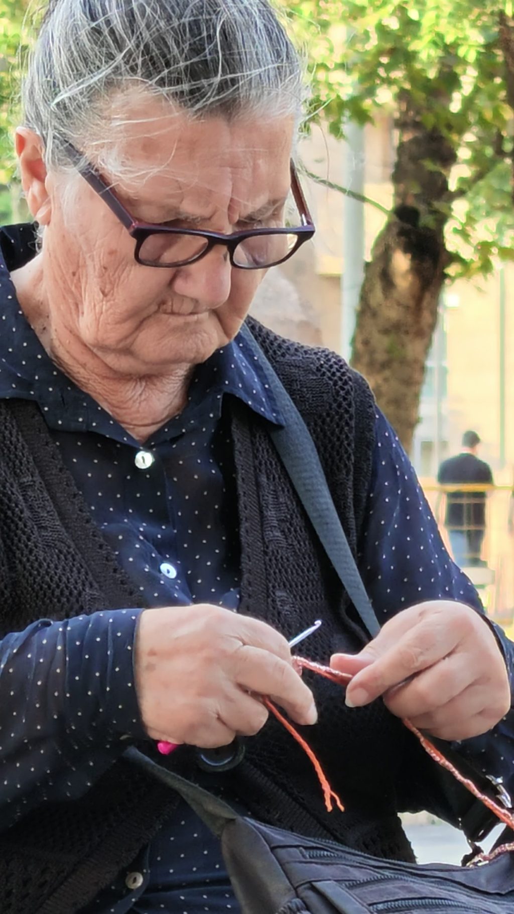 An older woman crocheting on a bench, working without looking up.