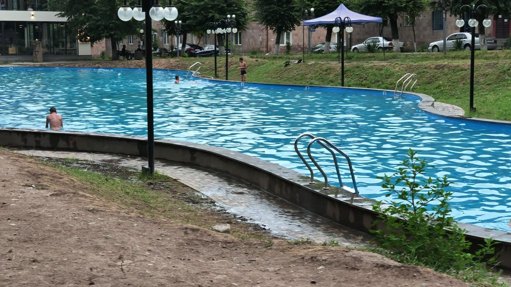 An open-air swimming pool in the park with mountains rising behind it.