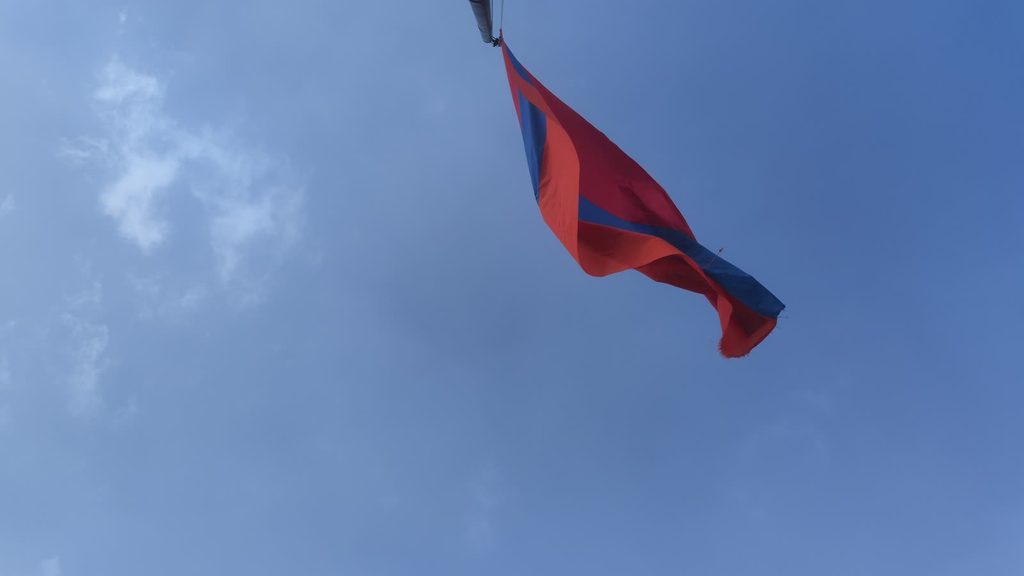 The red, blue and orange flag of Armenia flying against a blue sky with thin cloud.