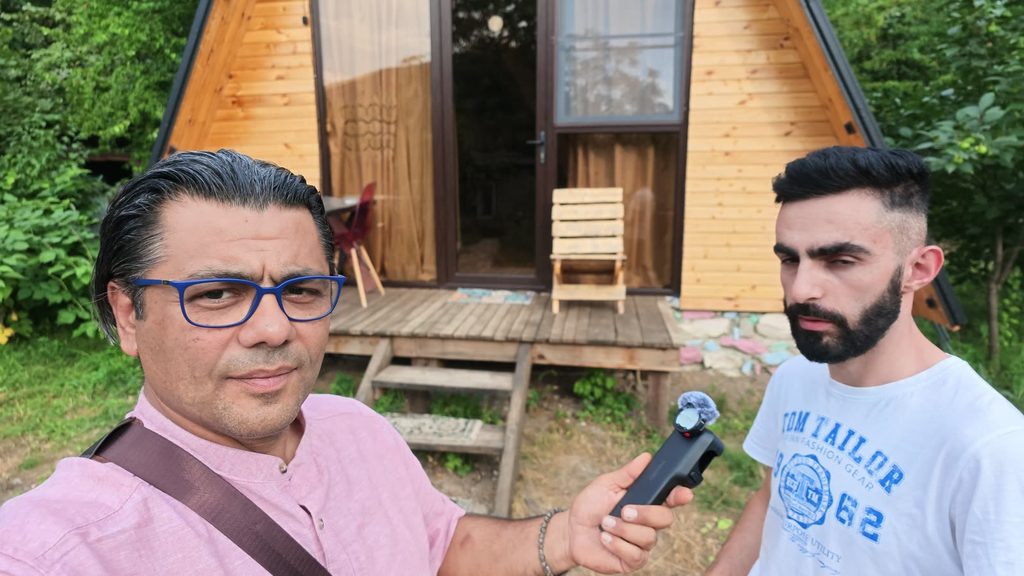 Nver standing outside the wooden cabin he built.