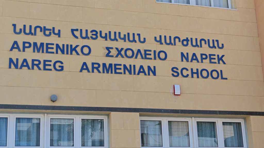 The name of the Nareg Armenian School in blue capitals on a pale stone wall, in Armenian, Greek and English, one line above the other.