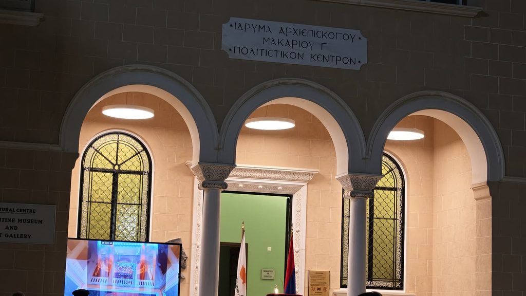 Three lit arches under a Greek sign for the Archbishop Makarios III Foundation's Cultural Centre, with the Cypriot and Armenian flags at the door and a screen in the foreground.