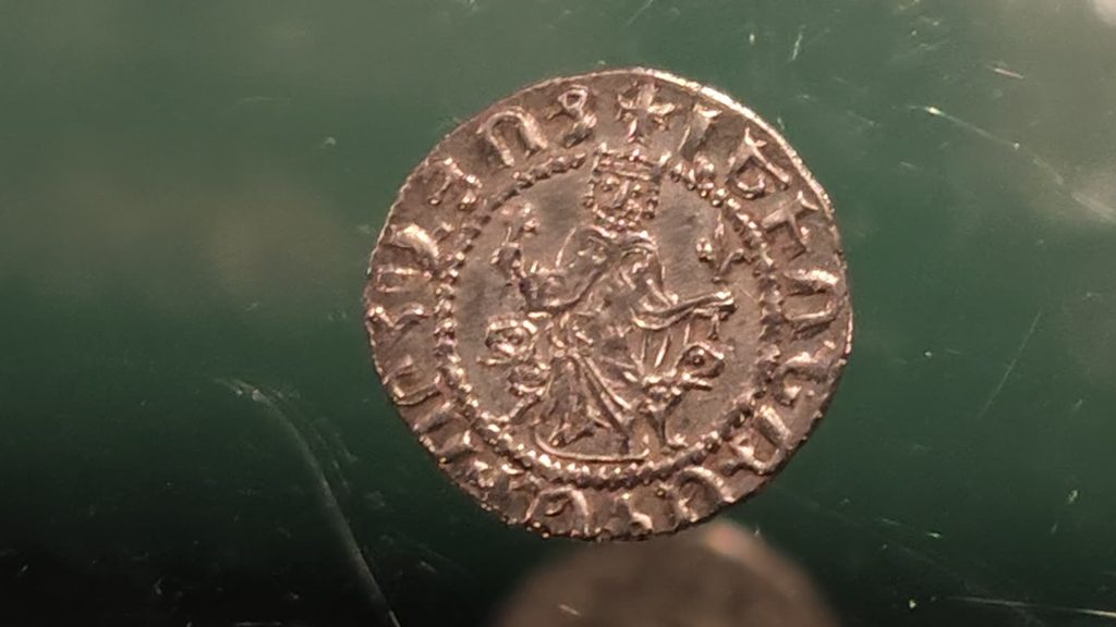 A worn silver coin showing an enthroned king, ringed by an Armenian inscription, on a dark green ground.